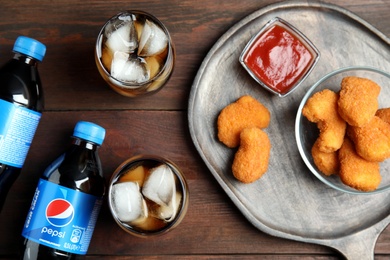 MYKOLAIV, UKRAINE - FEBRUARY 15, 2021: Glasses and bottles of Pepsi with snack on wooden table, flat lay