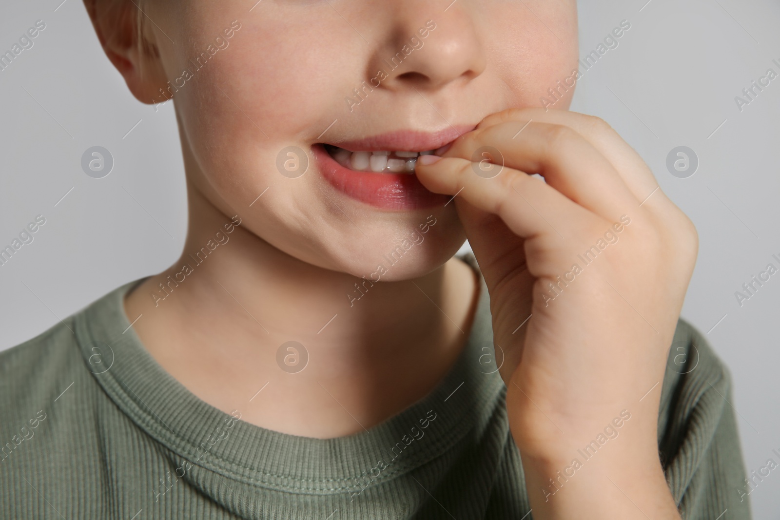 Photo of Little girl biting her nails on grey background, closeup