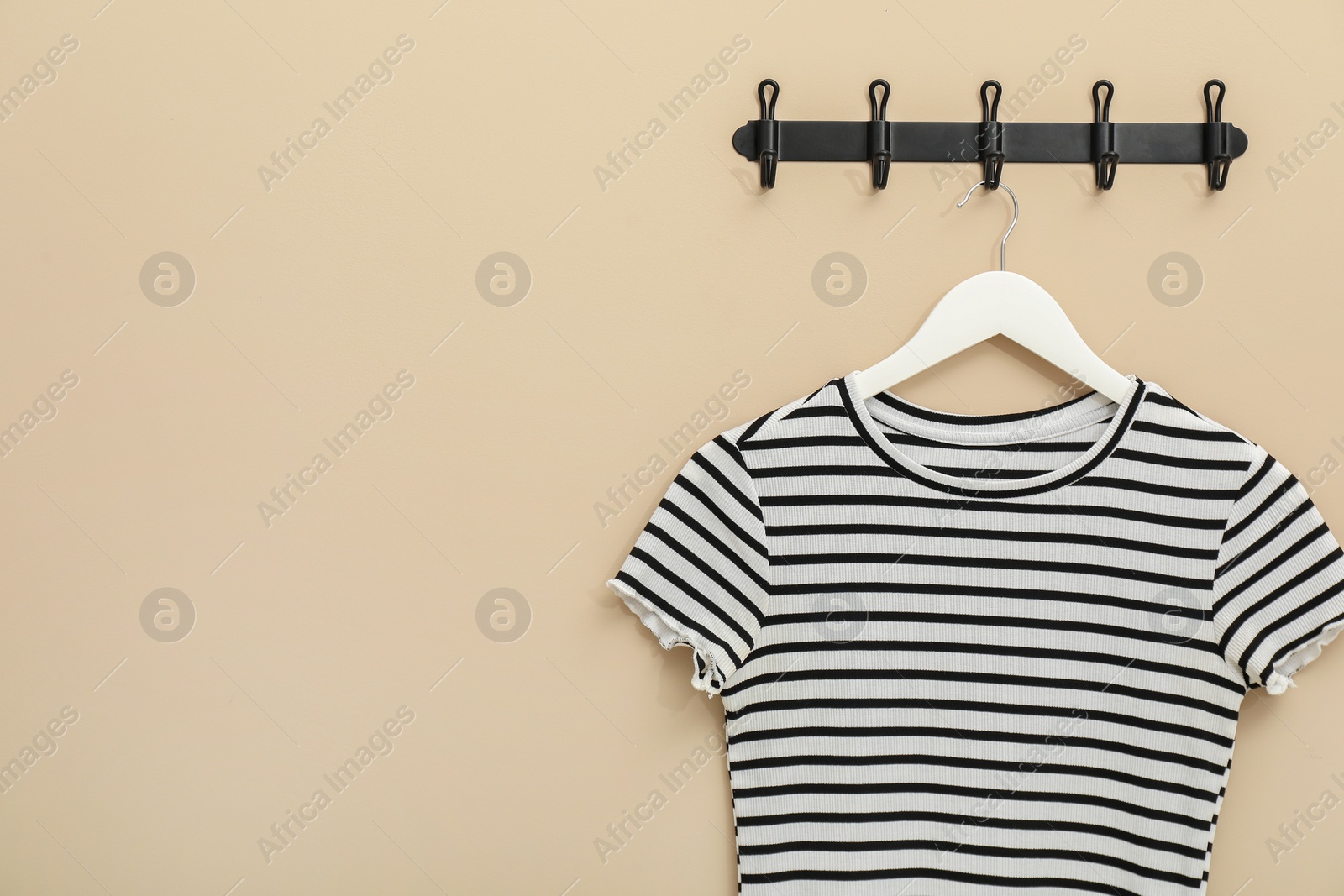 Photo of Hanger with striped t-shirt on beige wall, space for text