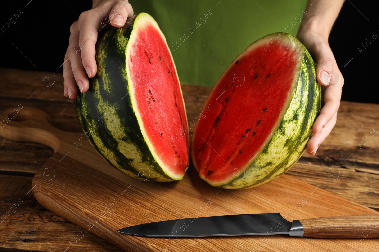 Photo of Woman with delicious halved watermelon at wooden table against black background, closeup