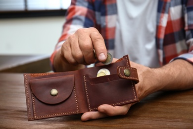 Senior man putting coin into purse at table, closeup