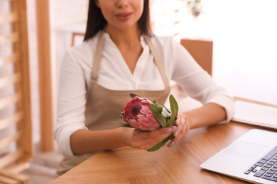 Photo of Florist with protea flower near laptop in store, closeup