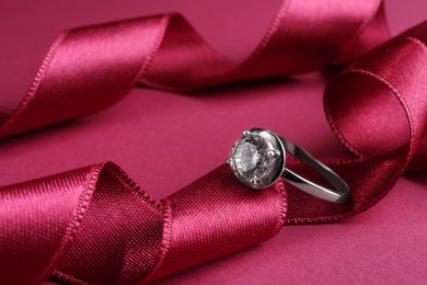 Photo of Beautiful luxury engagement ring with gemstone and ribbons on marsala background, closeup