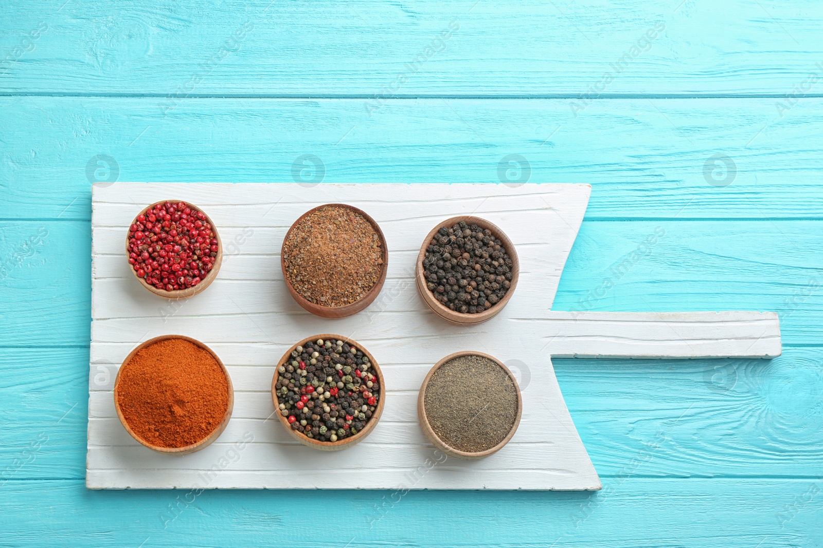 Photo of White board and bowls with different kinds of pepper on blue wooden table, top view