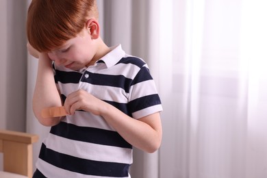 Little boy putting sticking plaster onto elbow indoors. Space for text