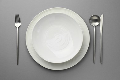 Clean dishes and cutlery on grey background, flat lay