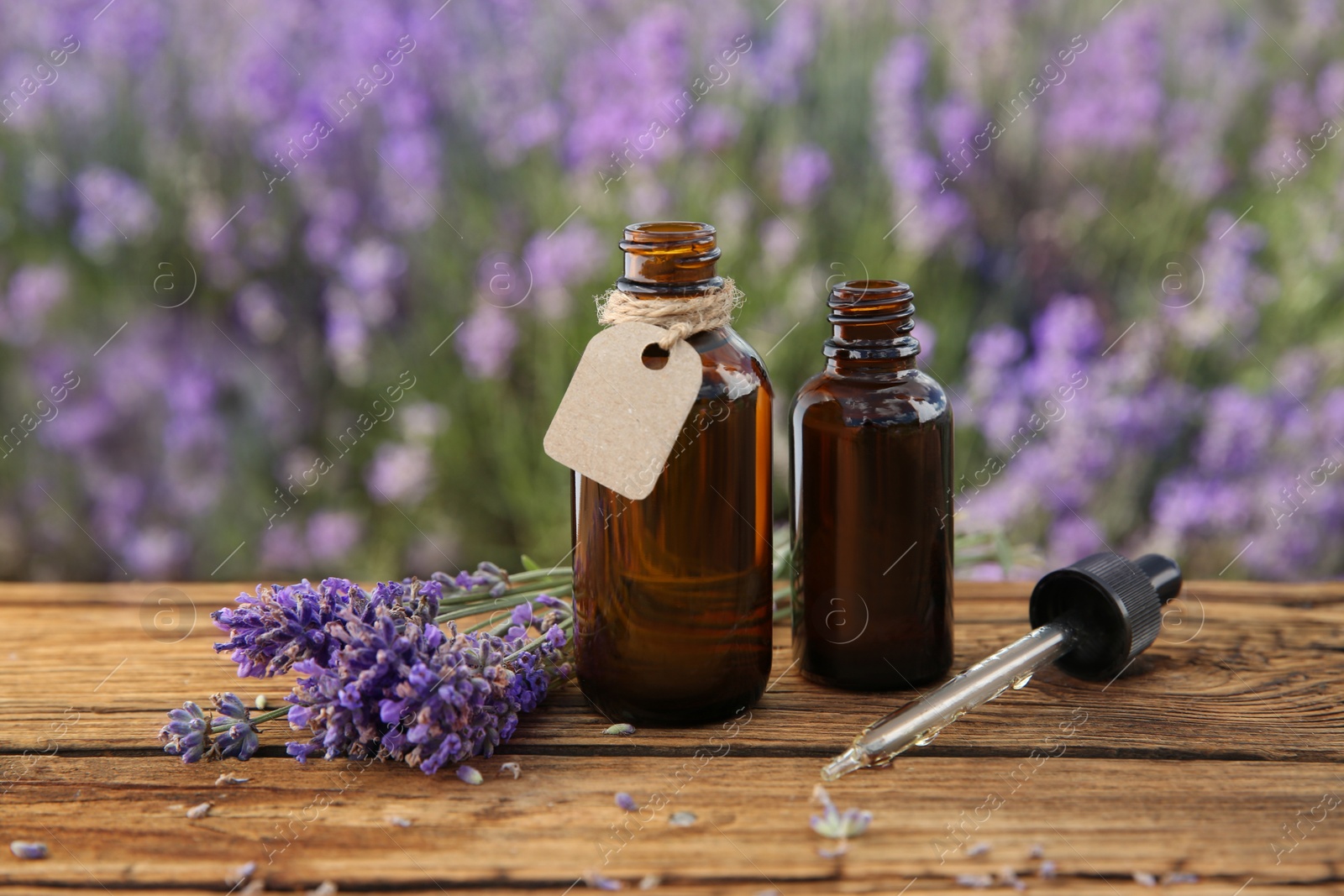 Photo of Bottles of natural essential oil, pipette and lavender flowers on wooden table