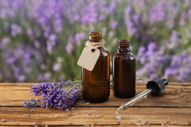 Photo of Bottles of natural essential oil, pipette and lavender flowers on wooden table