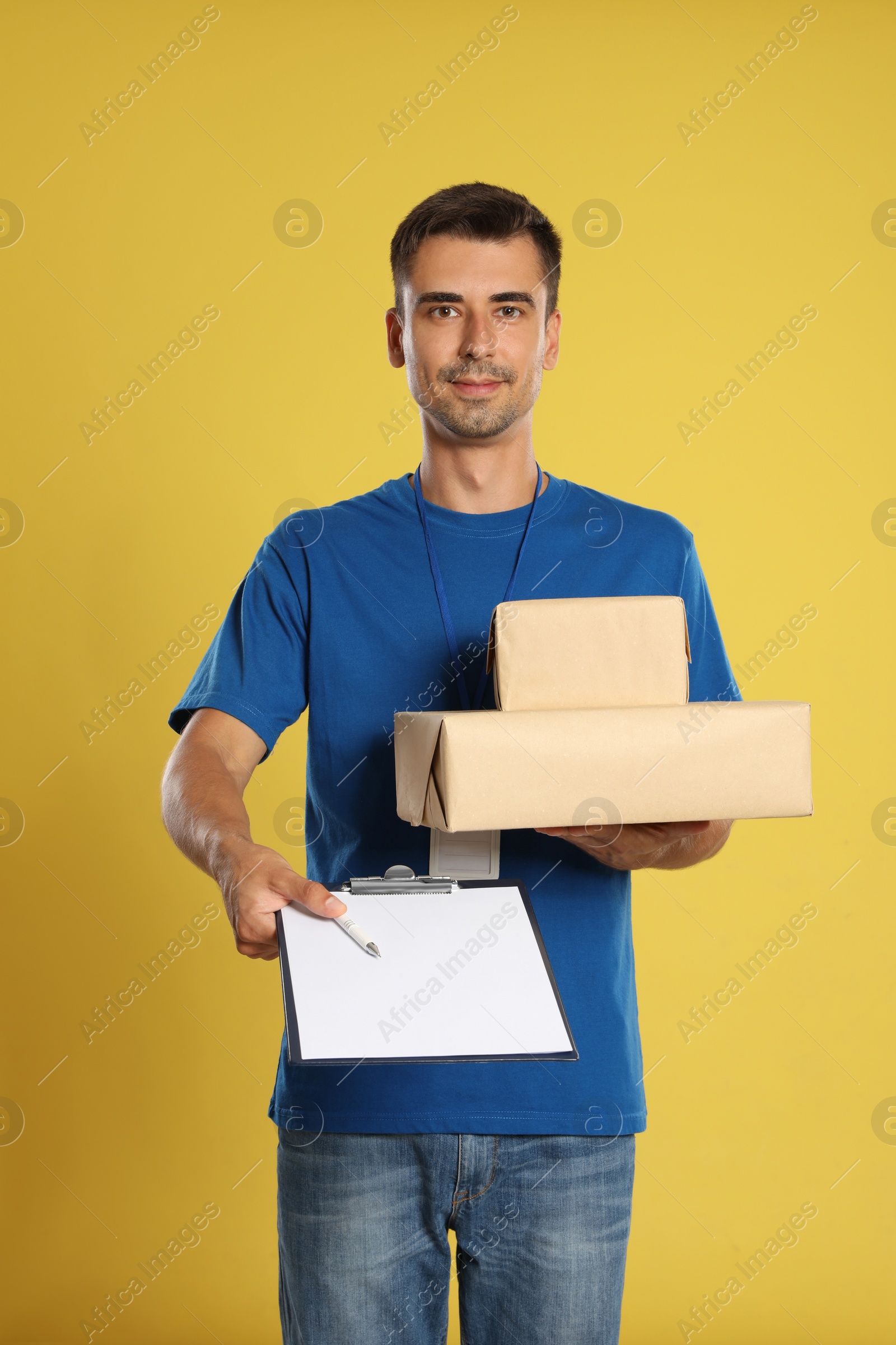 Photo of Happy young courier with parcels and clipboard on yellow background