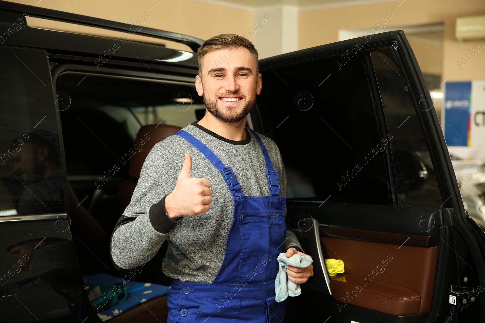 Photo of Smiling worker standing near car in shop. Window tinting service