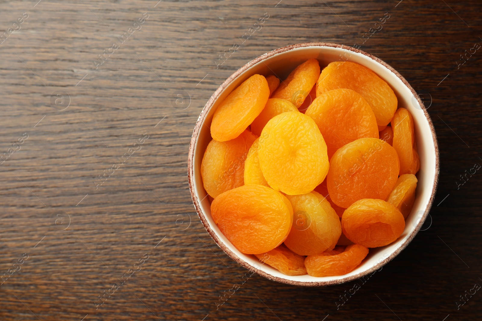 Photo of Bowl of tasty apricots on wooden table, top view and space for text. Dried fruits