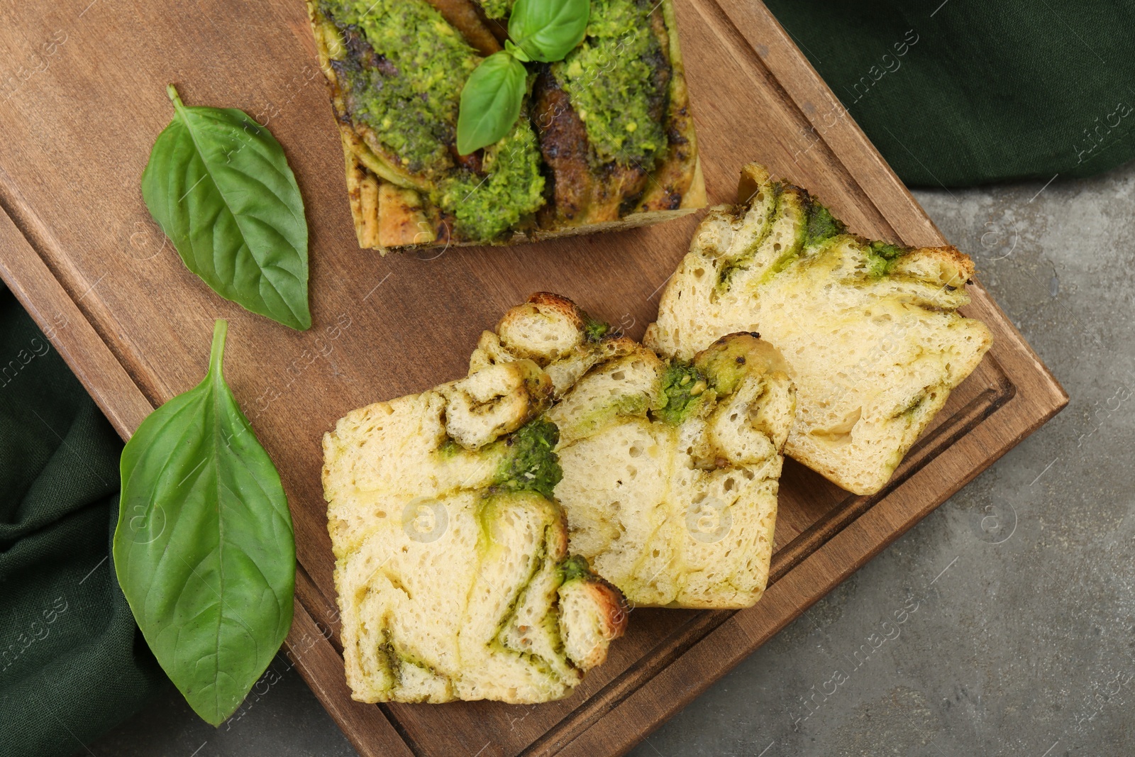 Photo of Freshly baked pesto bread with basil on grey table, flat lay