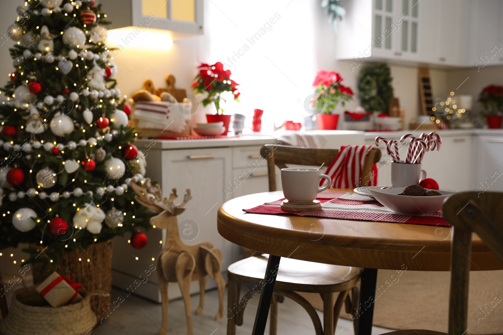 Photo of Cup of drink and candy canes on wooden table near Christmas tree in kitchen interior