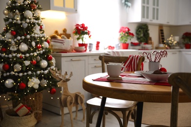 Photo of Cup of drink and candy canes on wooden table near Christmas tree in kitchen interior