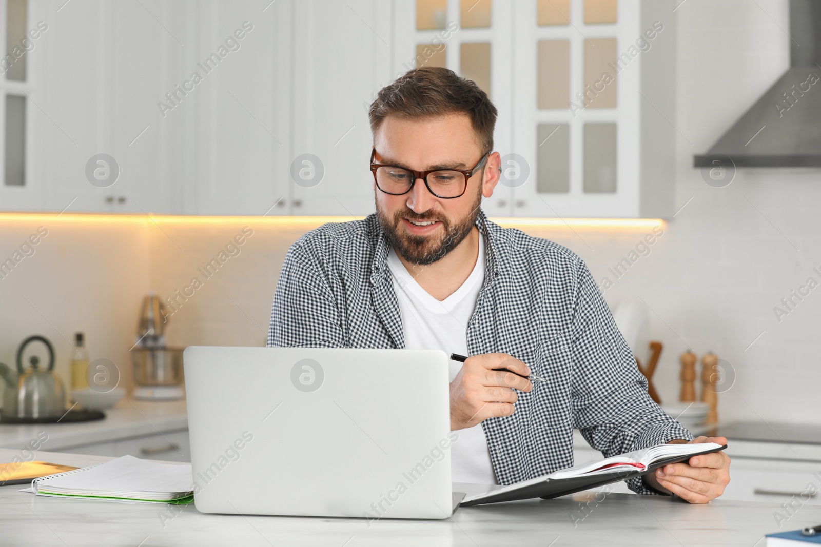 Photo of Young man working with notebook and laptop at home