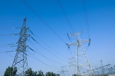 Photo of High voltage towers against blue sky on sunny day, low angle view