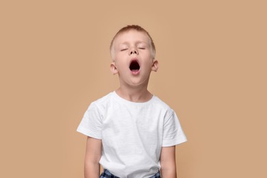 Photo of Sleepy boy yawning on beige background. Insomnia problem