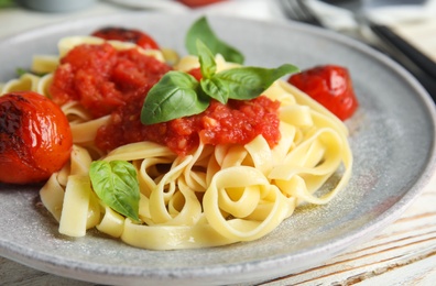 Tasty pasta with tomatoes and basil on white wooden table, closeup