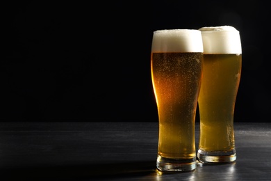 Photo of Glasses of cold tasty beer on dark background