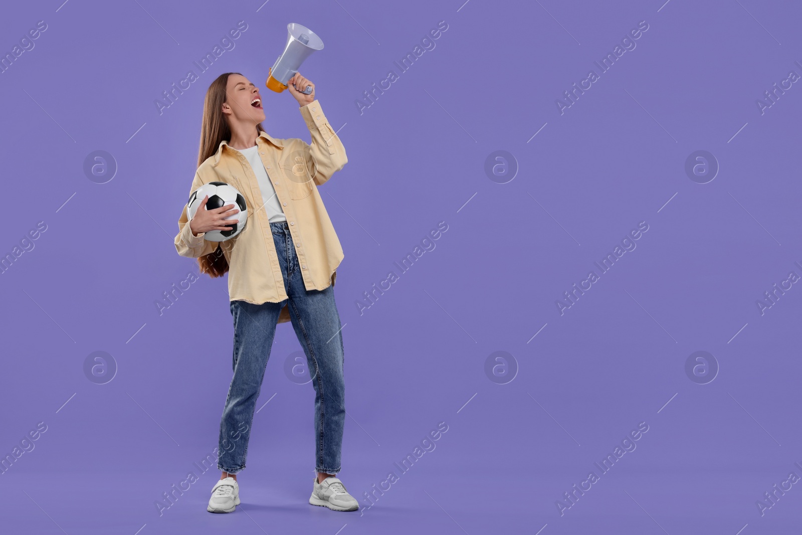 Photo of Emotional sports fan with ball and megaphone on purple background. Space for text