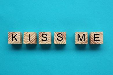 Photo of Wooden cubes with phrase Kiss Me on light blue background, flat lay