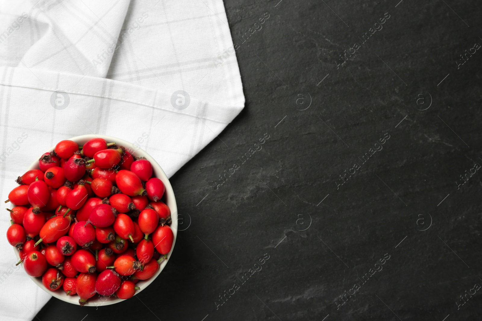 Photo of Ceramic bowl with rose hip berries on black table, top view and space for text. Cooking utensil