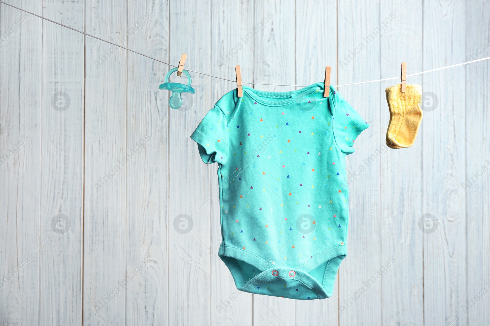 Photo of Bodysuit, pair of socks and pacifier on laundry line against wooden background, space for text. Baby accessories