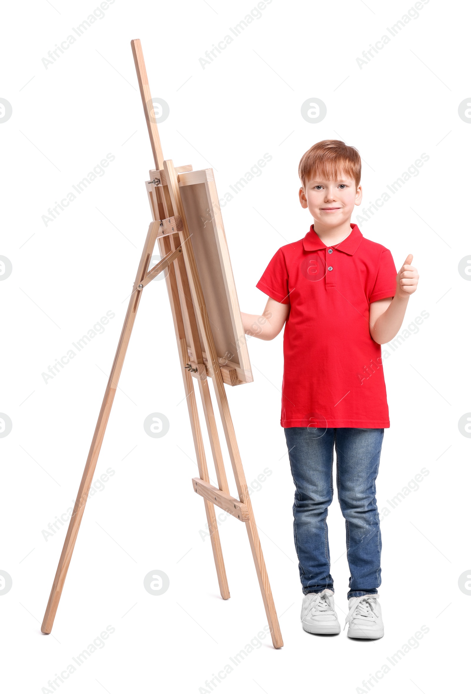 Photo of Little boy with brush near easel with canvas showing thumbs up against white background. Creative hobby