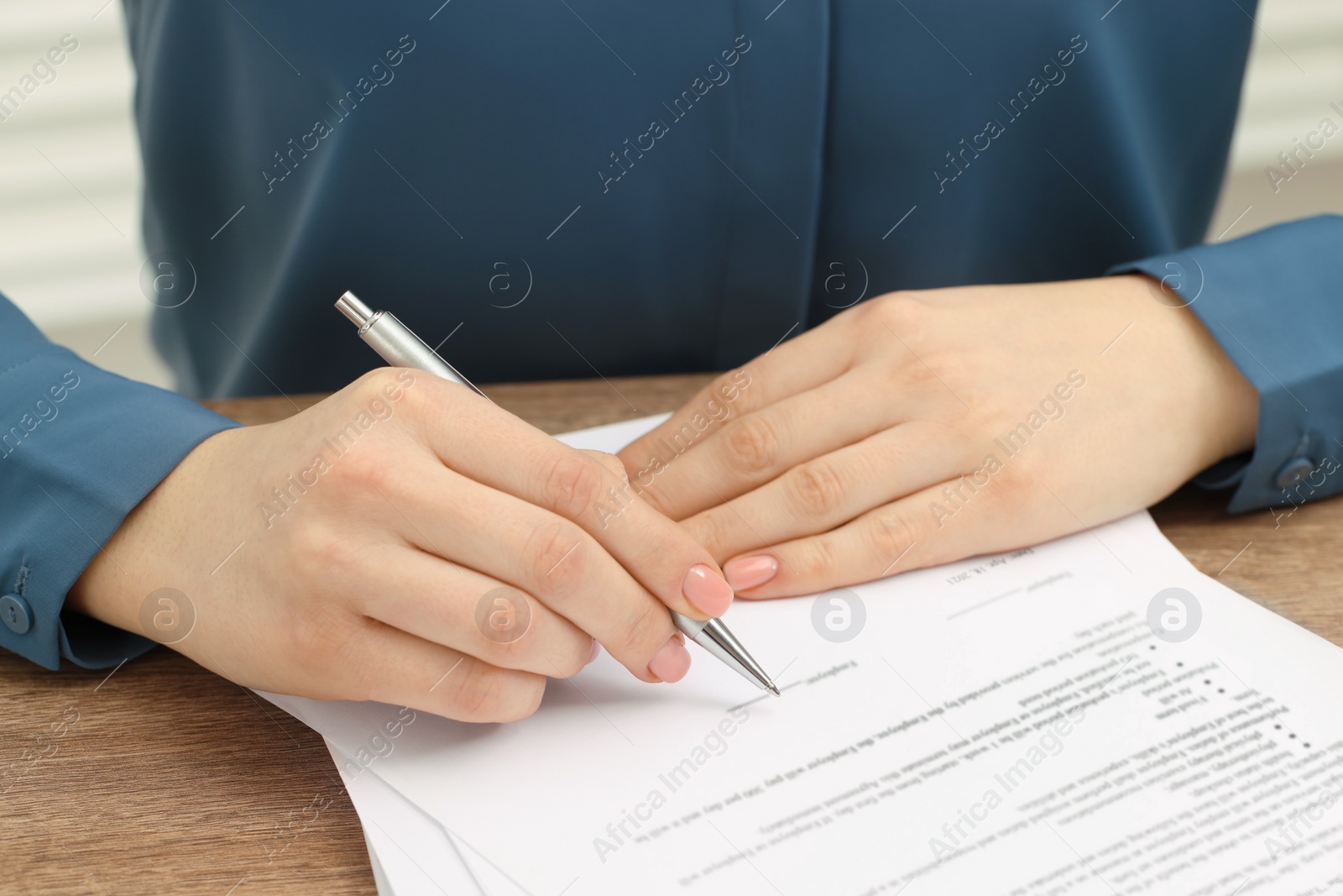 Photo of Woman signing document at wooden table, closeup