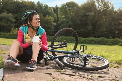 Photo of Young woman with injured knee near bicycle outdoors