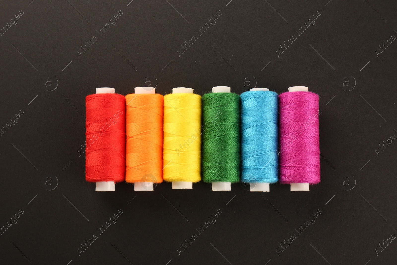 Photo of Different colorful sewing threads on black background, flat lay