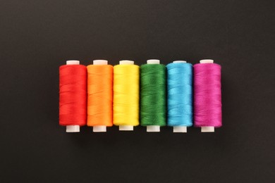 Different colorful sewing threads on black background, flat lay