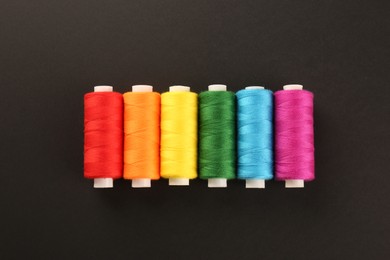 Photo of Different colorful sewing threads on black background, flat lay