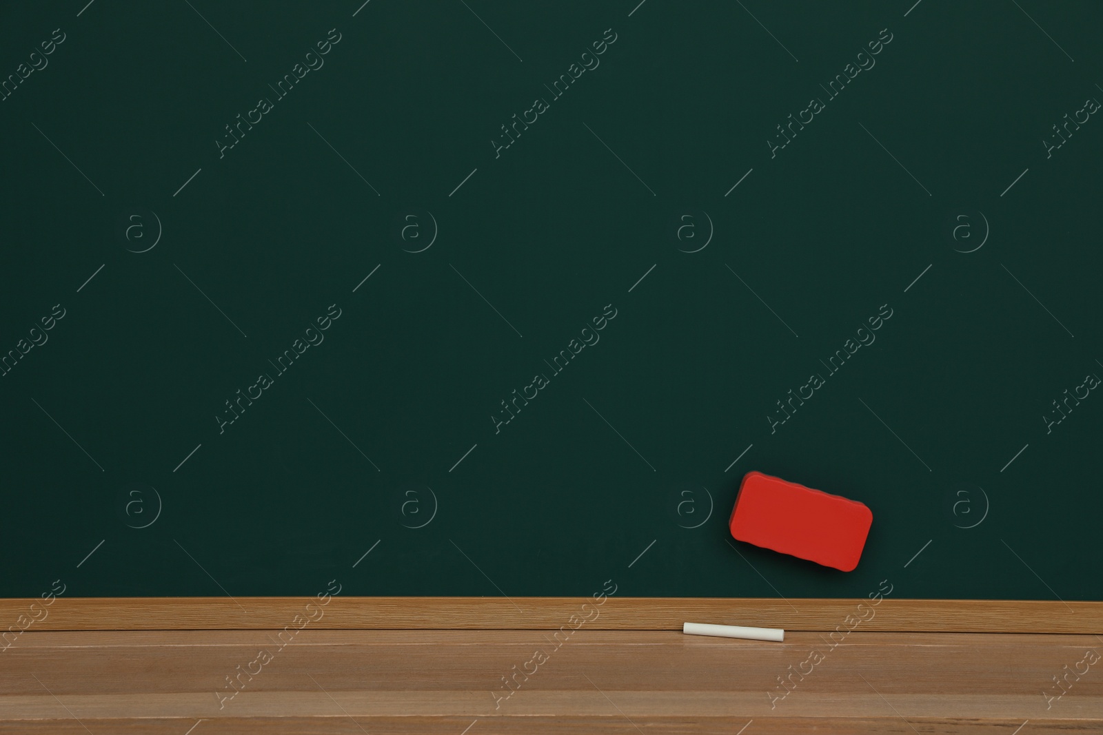 Photo of Piece of chalk and duster on wooden table near greenboard space for text