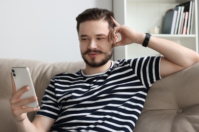 Photo of Smiling man using smartphone on beige sofa in cozy room