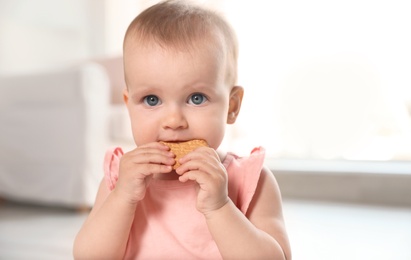 Photo of Portrait of cute baby girl with cookie in room