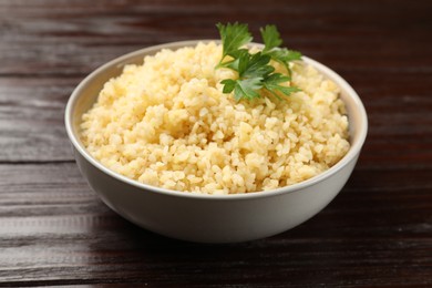 Photo of Delicious bulgur with parsley in bowl on wooden table, closeup