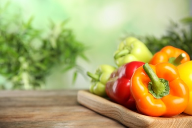 Photo of Board with ripe bell peppers on wooden table against blurred background, space for text