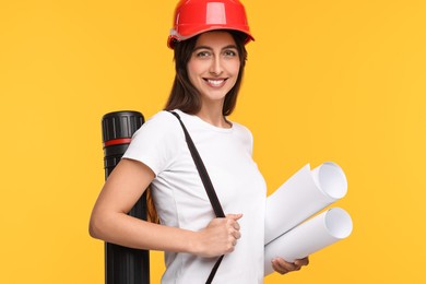 Photo of Architect in hard hat with drafts and tube on yellow background