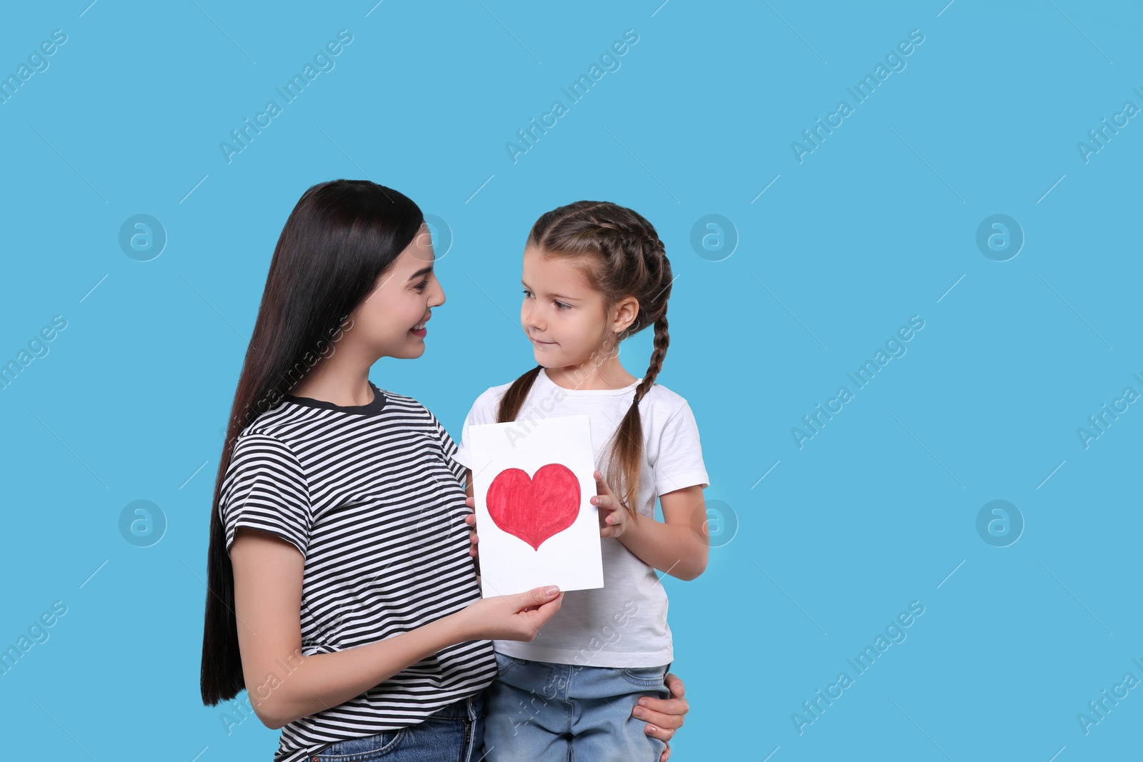 Photo of Happy woman with her cute daughter and handmade greeting card on light blue background, space for text. Mother's day celebration