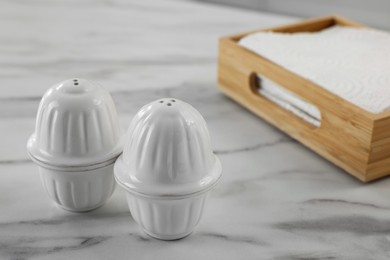 Photo of Ceramic salt and pepper shakers near box of napkins on white marble table in kitchen. Space for text