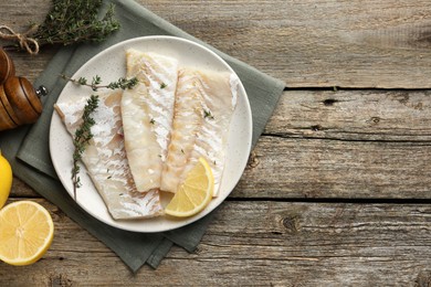 Photo of Fresh raw cod fillets with thyme and lemon on wooden table, flat lay. Space for text