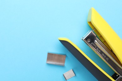 Yellow stapler with staples on light blue background, top view. Space for text