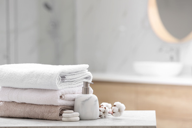 Photo of Clean towels, spa stones and soap dispenser on table in bathroom. Space for text