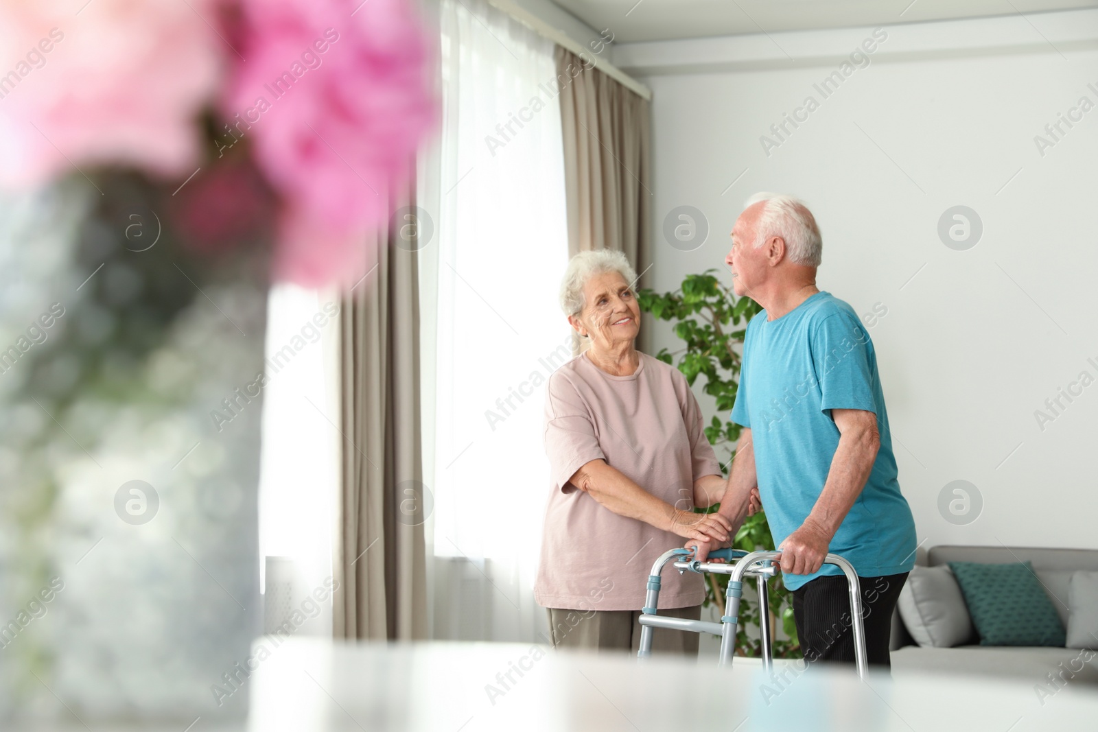 Photo of Elderly woman and her husband with walking frame indoors