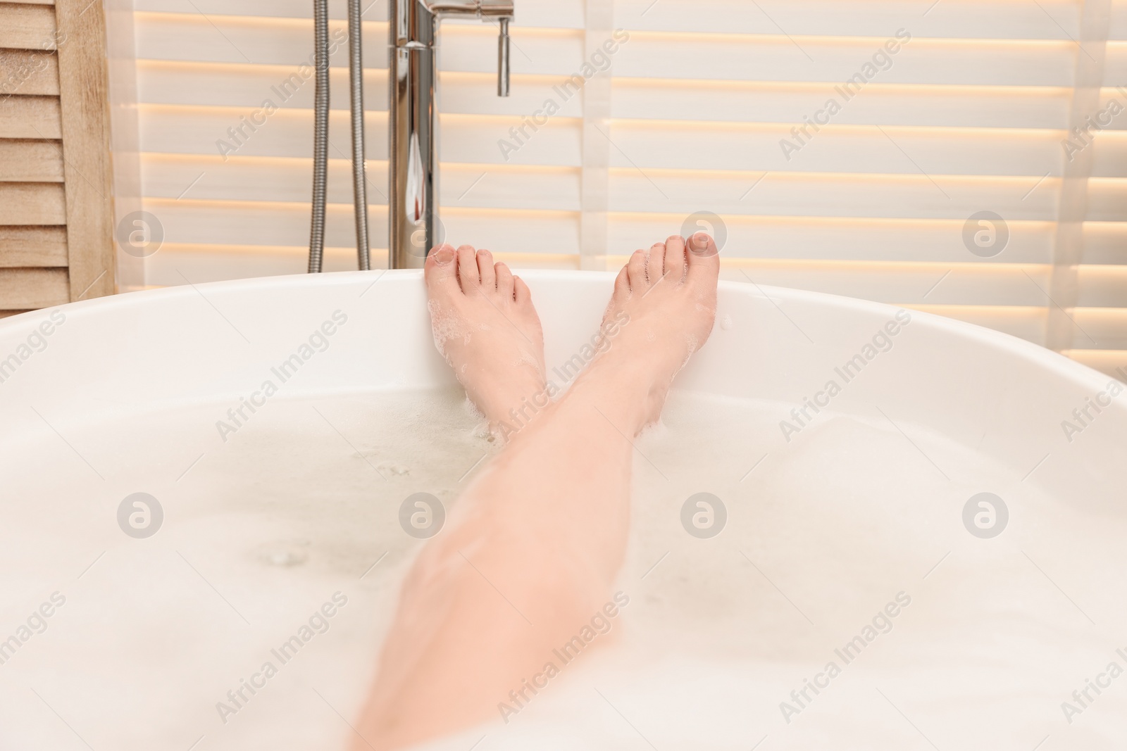 Photo of Woman taking bath with foam in tub indoors, closeup