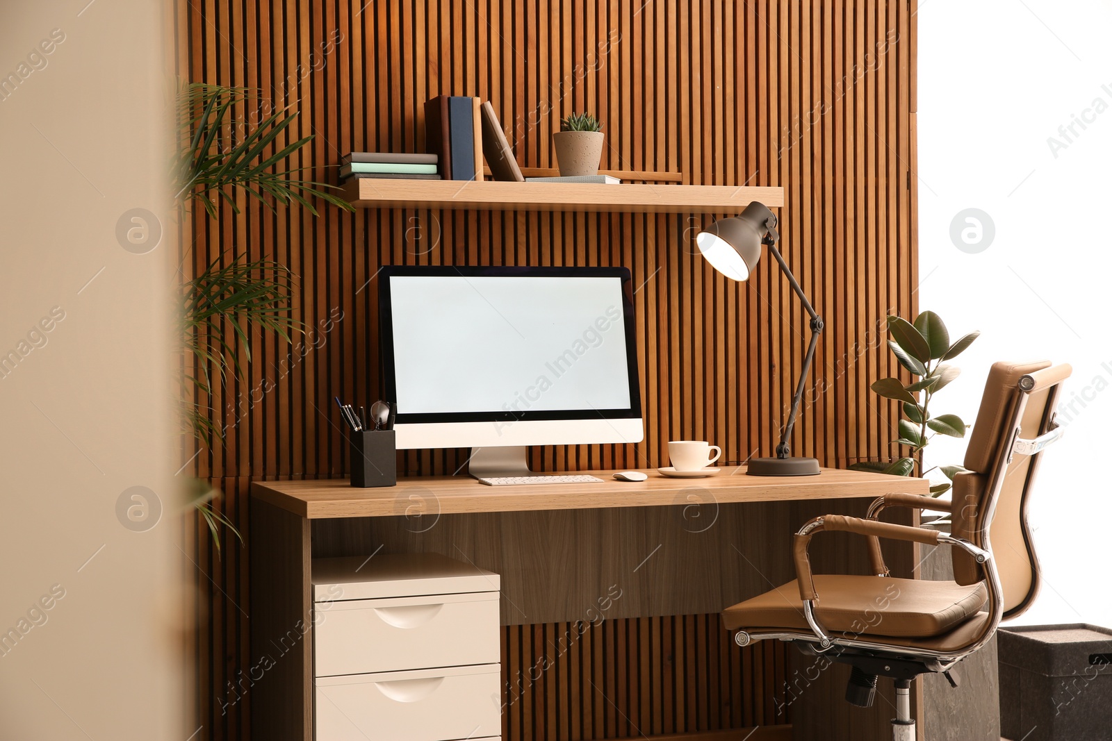 Photo of Comfortable workplace with computer near wooden wall in stylish room interior. Home office design