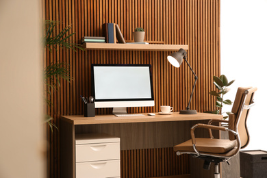 Photo of Comfortable workplace with computer near wooden wall in stylish room interior. Home office design