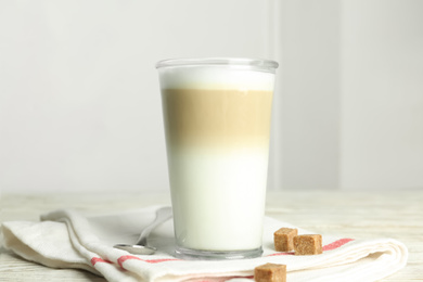Delicious latte macchiato and sugar cubes on white wooden table indoors