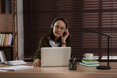 Photo of Woman with modern laptop and headphones learning at table indoors